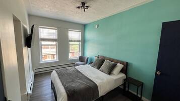 A bedroom with a bed, a chair, a heater, and a door.