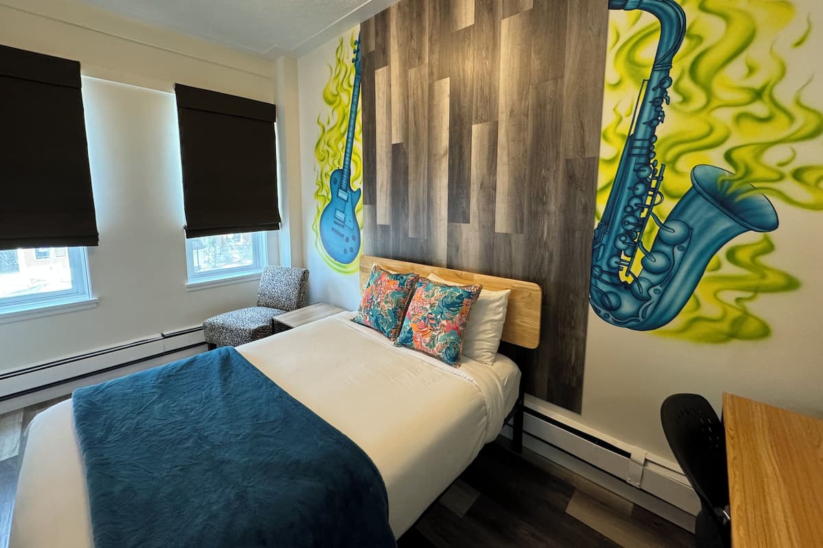 A modern bedroom with a bed, a wall mural of saxophones, and a window with blinds.
