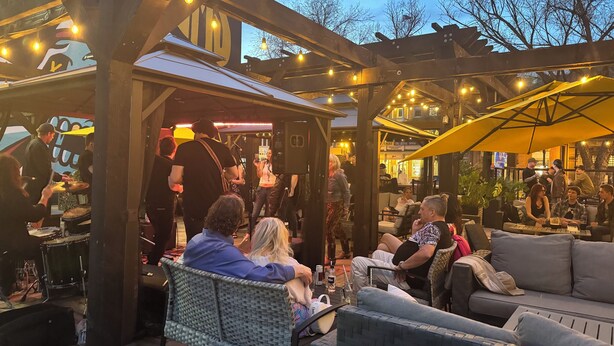 Een terras buiten met zitplaatsen en een podium voor live muziek.