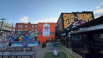 Un espace extérieur aménagé avec des tables et des chaises, une fresque sur le bâtiment et une enseigne indiquant « CRUSH BEERS & DREAMS ».
