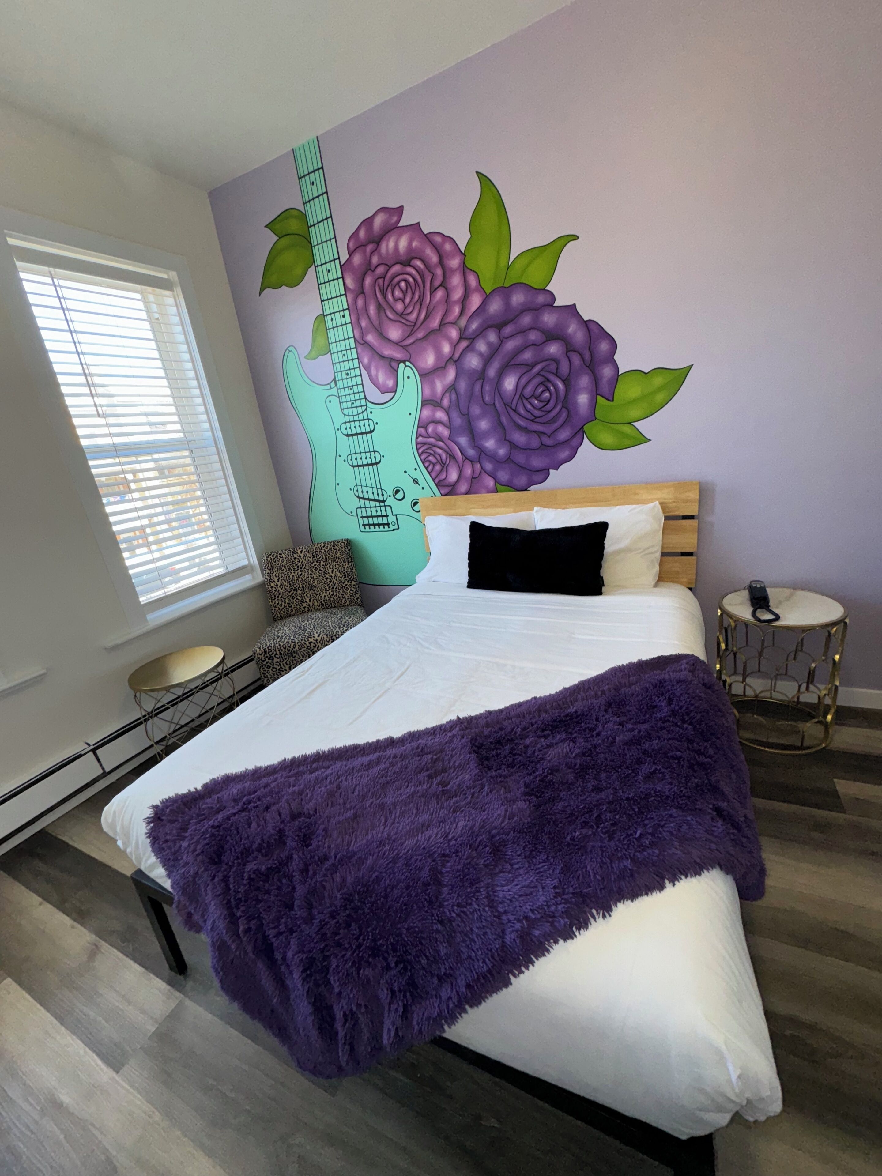 Un dormitorio con una cama, un edredón morado, un mural de una guitarra y una ventana con persianas.