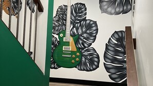 Een trap met een groene leuning, een houten vloer en een muur met een groot muurschildering van een groene gitaar en zwarte bladeren.
