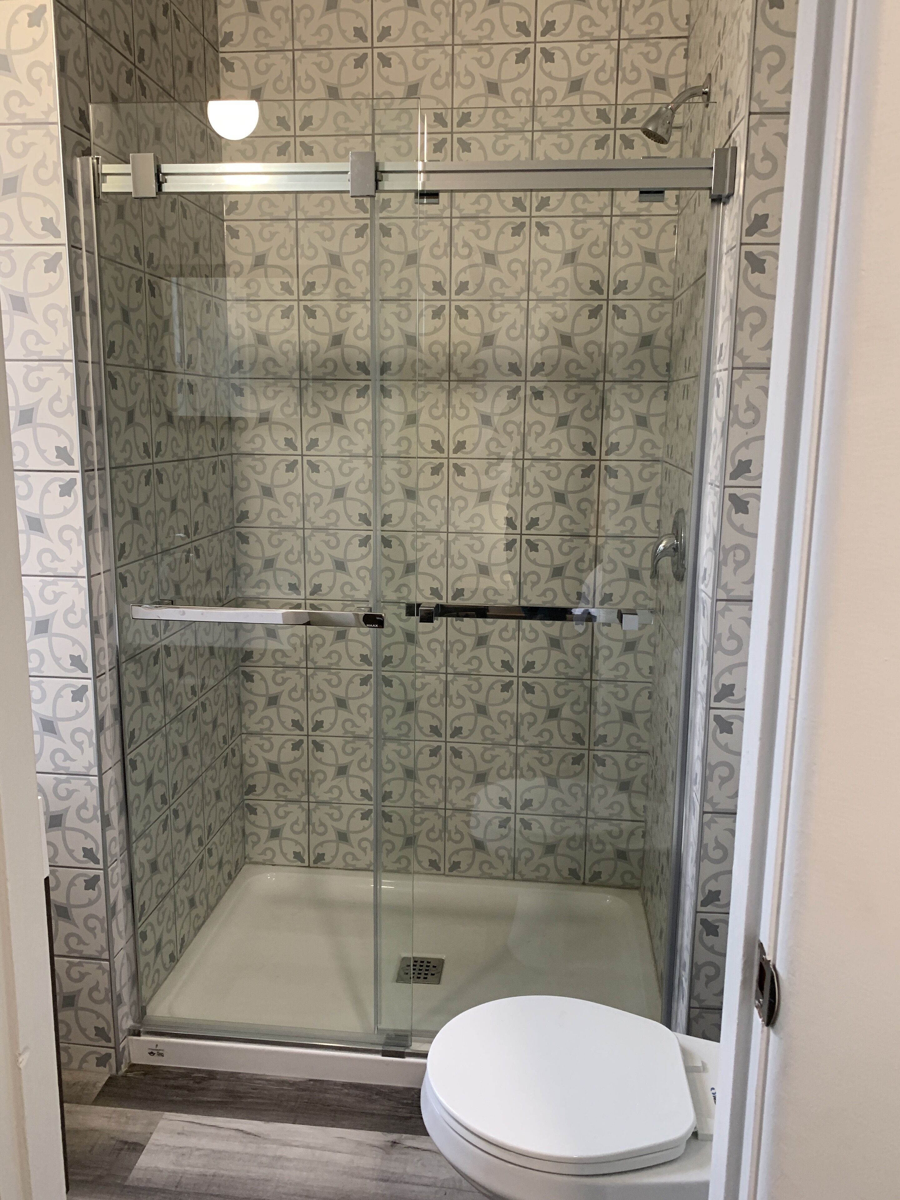 Cabina doccia con pareti in vetro e un water bianco in un bagno con piastrelle decorate.