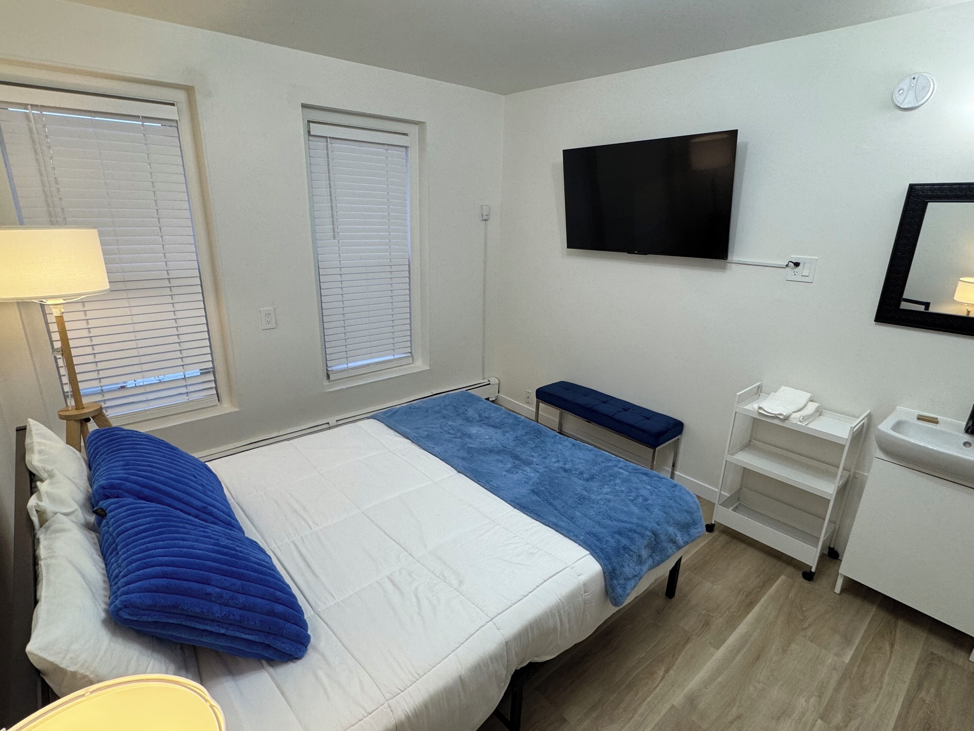 Una habitación de hotel con una cama, un banco, un televisor, un lavabo y un espejo.