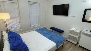 Una habitación de hotel con una cama, un banco, un televisor, un lavabo y un espejo.