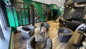 Een hal met leren fauteuils, een ronde tafel en een groene wand met bladmotieven.