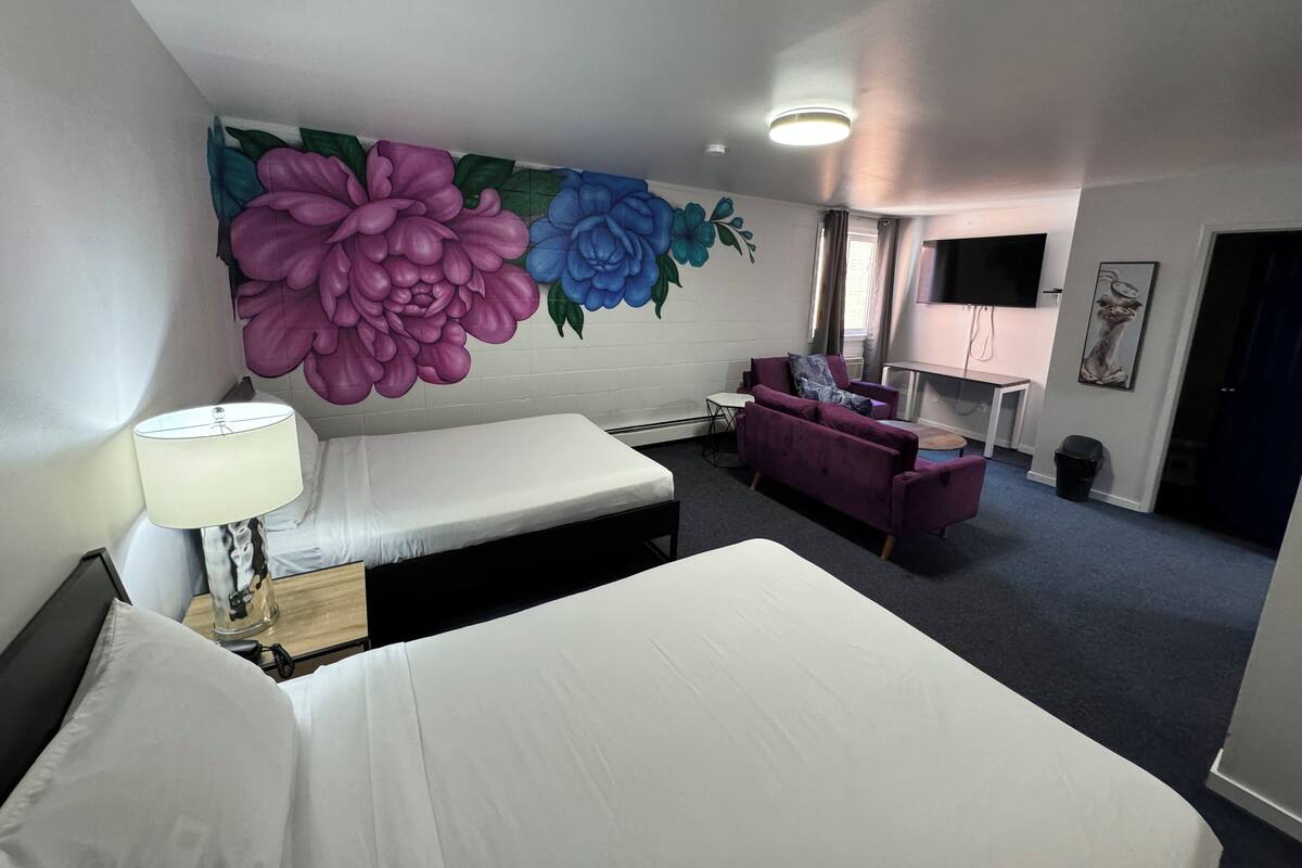 A hotel room with two beds, a sofa, a desk, and a large floral mural on the wall.