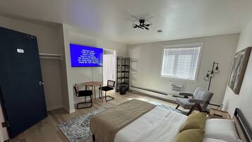 Un dormitorio con cama, escritorio, silla, televisor y ventilador de techo.