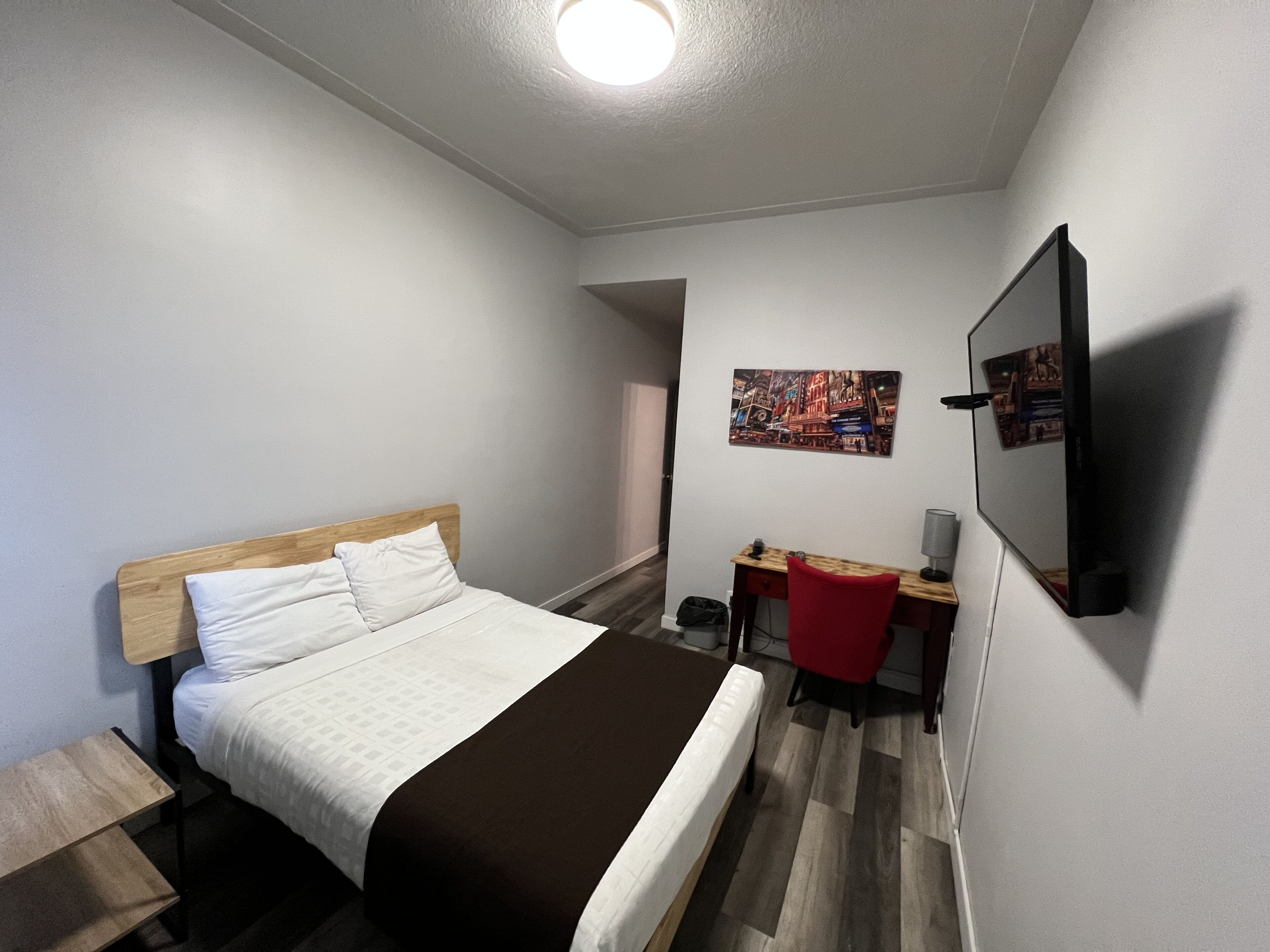 Ein Hotelzimmer mit Bett, Schreibtisch, Stuhl, Fernseher und einem Bild an der Wand.