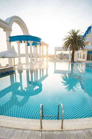 Una piscina con diseño de ajedrez, rodeada de columnas blancas y una palmera.