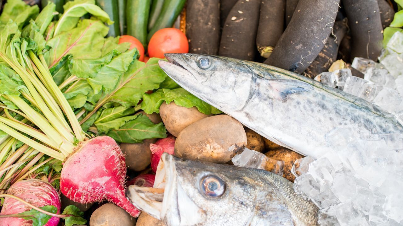 Une grande variété de produits frais, notamment des légumes-feuilles, des radis et du poisson entier, présentés sur de la glace.