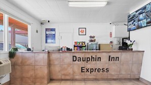 A reception desk at Dauphin Inn Express with a check-out counter, a small refrigerator, snacks, and a mounted security camera. - Dauphin Inn Express (Dauphin)