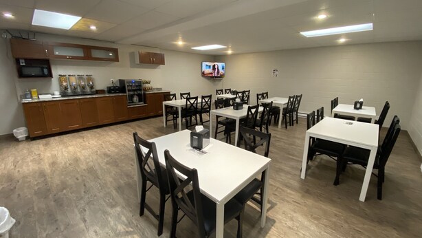 A dining area with multiple tables and chairs, a kitchen area with a microwave and refrigerator, and a television on the wall. - Dauphin Inn Express (Dauphin)