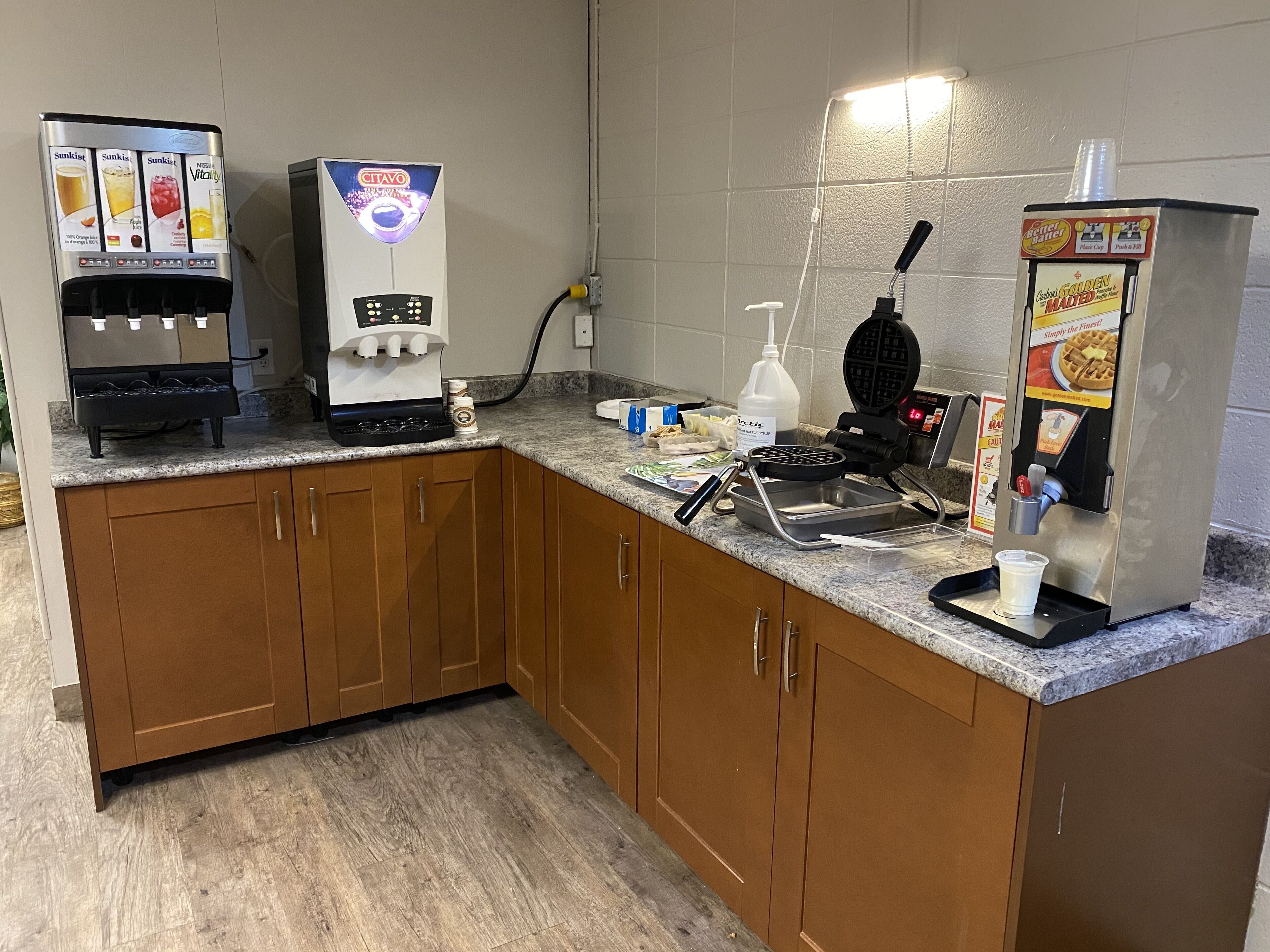 Angolo cottura con macchina da caffè, piastra per waffle e dispenser per condimenti.