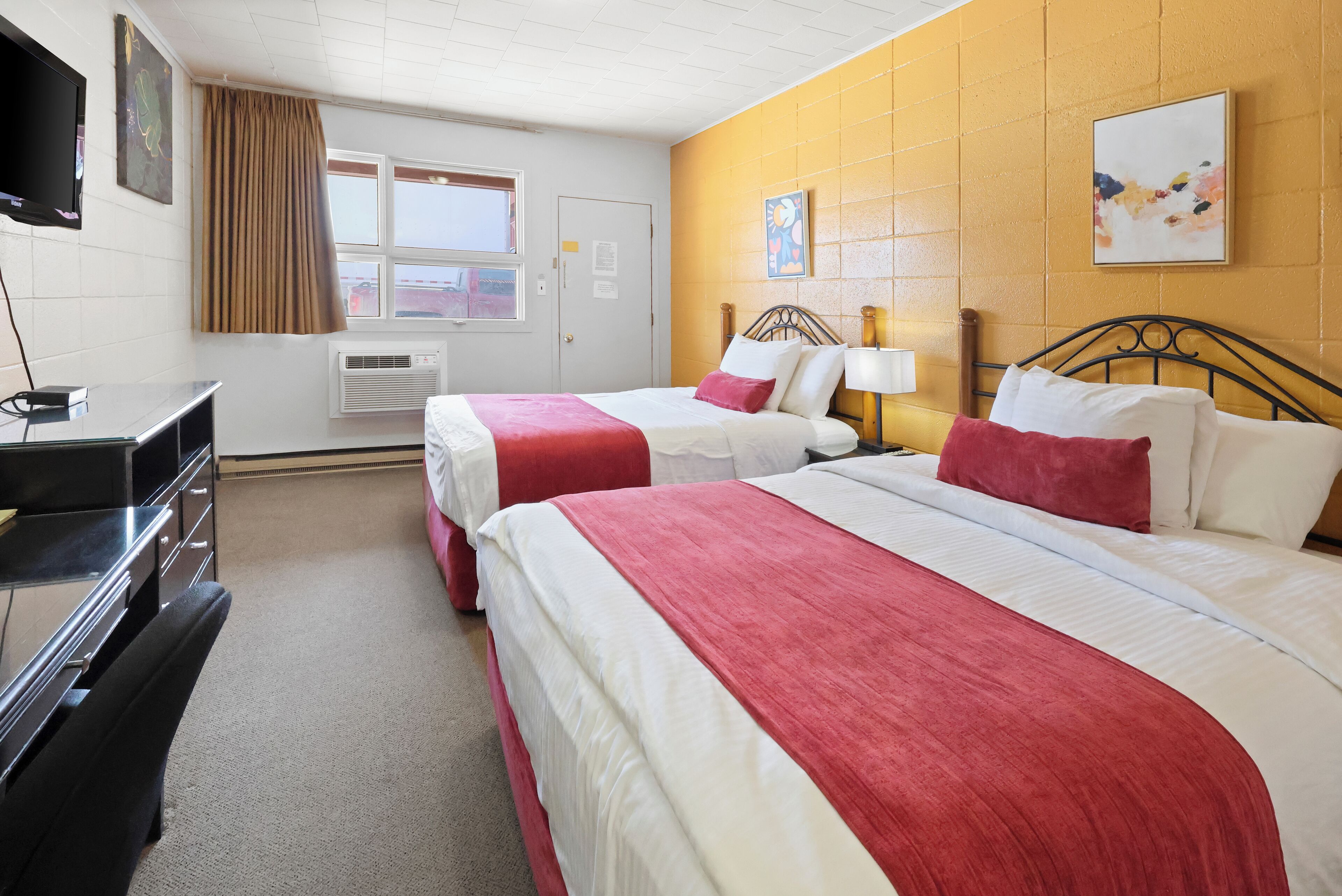 A hotel room with two beds, a desk, and a TV.