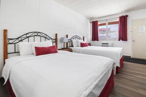 A hotel room with two beds, white bedding, red accents, a window with curtains, and a door with a lock.