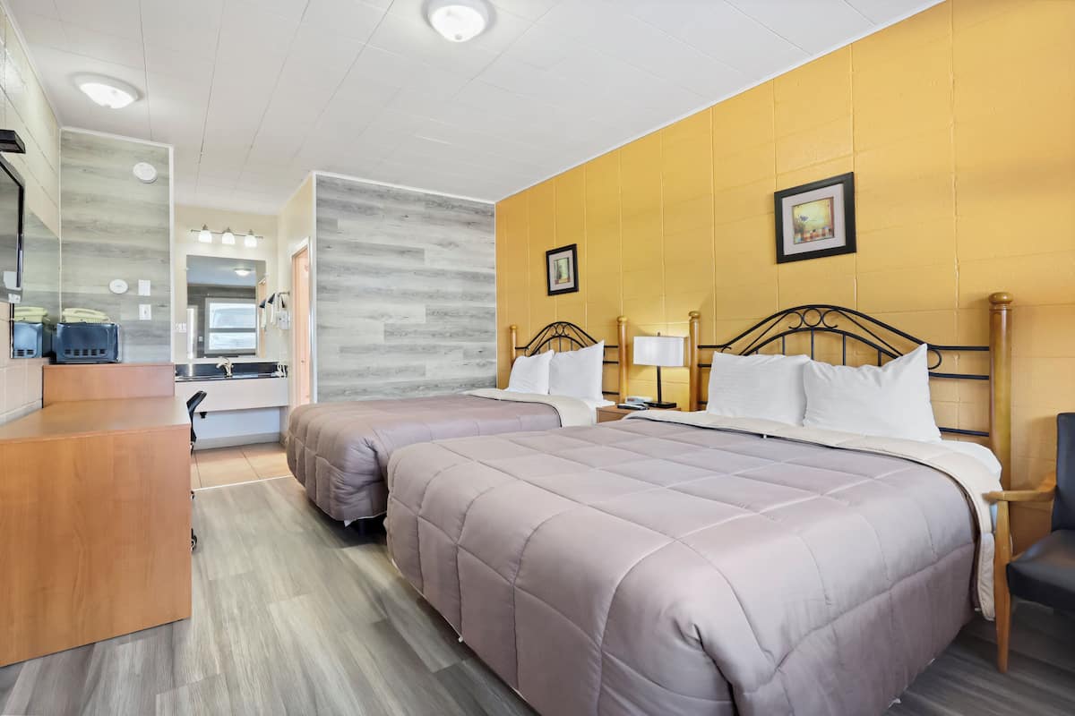 Une chambre d’hôtel avec deux lits, un bureau en bois, un miroir et une salle de bain visible à travers une porte ouverte.