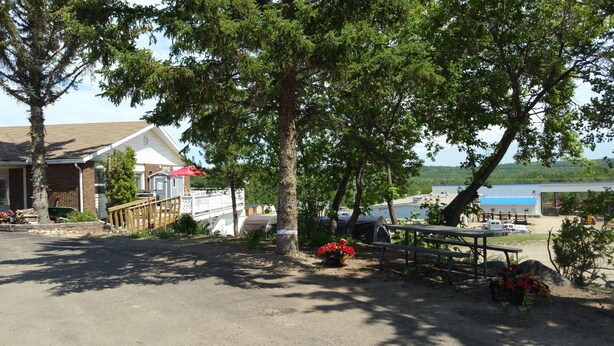 A rustic cabin with a porch, a covered picnic table, and a red umbrella. - Athabasca Lodge Motel (Athabasca)