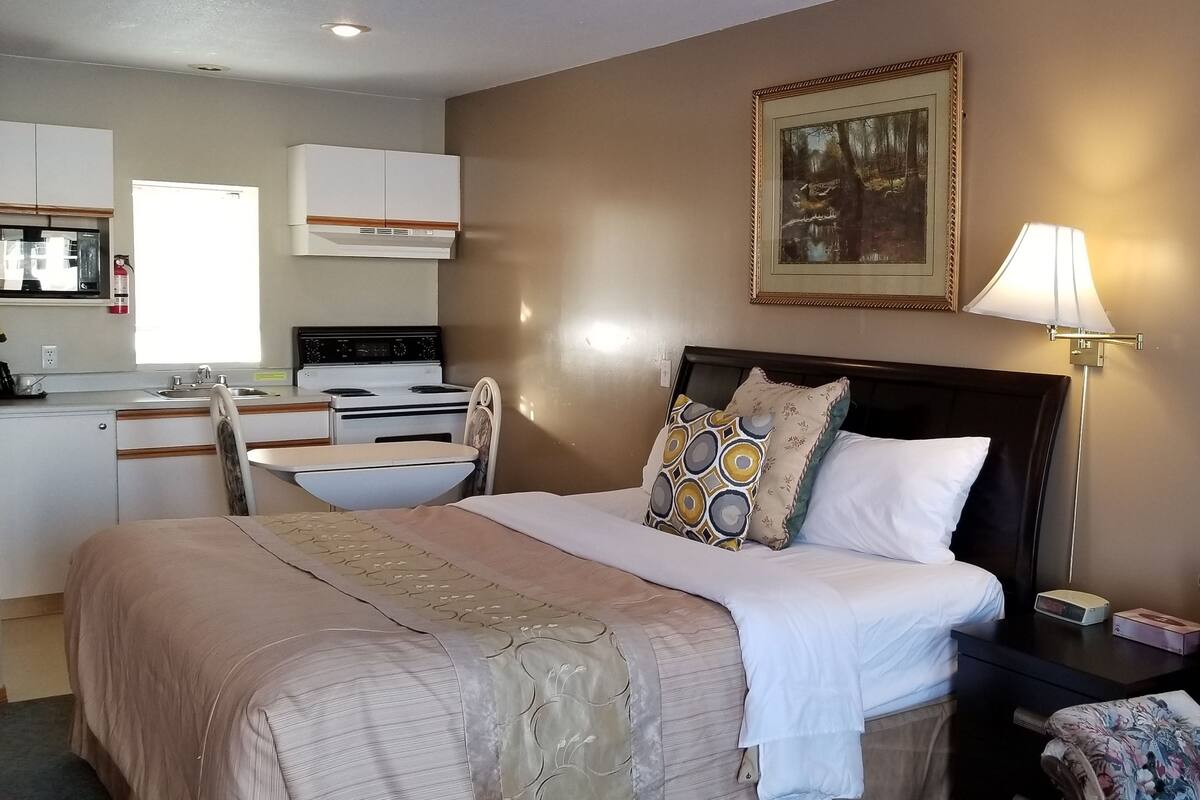 A hotel room with a bed, bedside table, chair, and a kitchenette area.