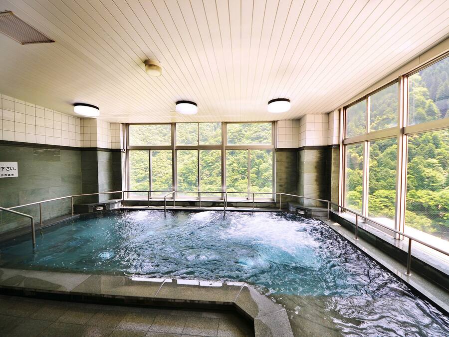 Un bain dans une source thermale, avec vue sur une zone boisée grâce à de grandes fenêtres.