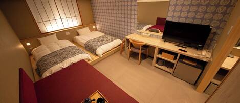 A hotel room with two beds, a desk with a TV, a small kitchenette, and a sliding shoji screen.
