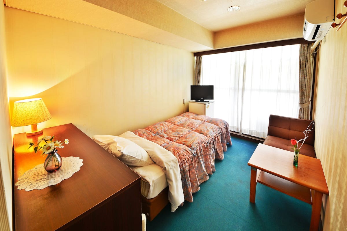 A hotel room with a bed, a desk, a chair, a TV, and a window with curtains.