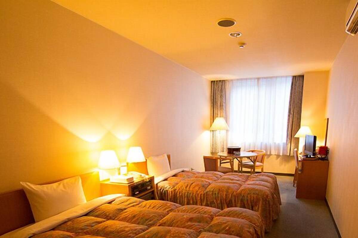 A hotel room with two beds, a desk with a chair, a lamp, and a window with curtains.