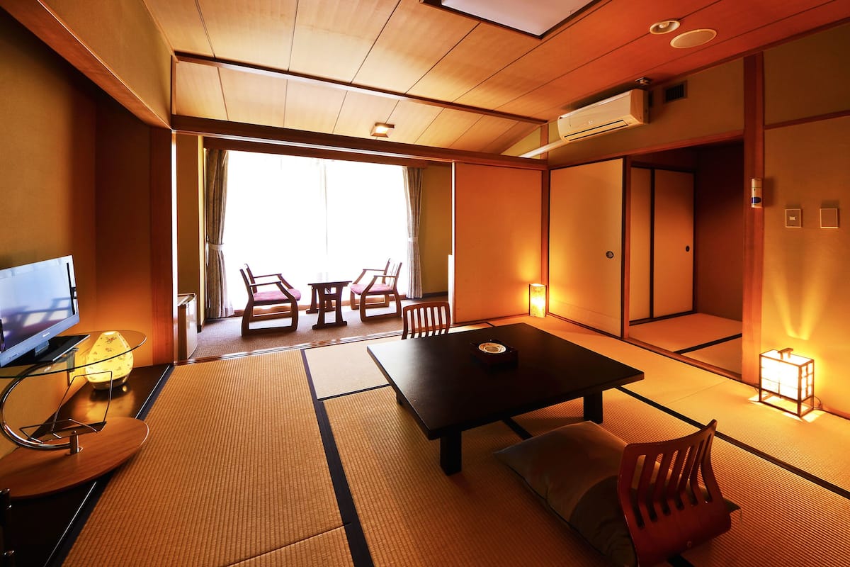 A traditional Japanese room with tatami flooring, a low table, a TV, and a sliding door leading to a balcony.