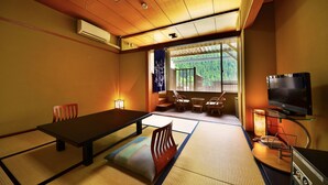 Una habitación japonesa tradicional con suelo de tatami, una mesa baja, un televisor y vistas al exterior con vegetación.