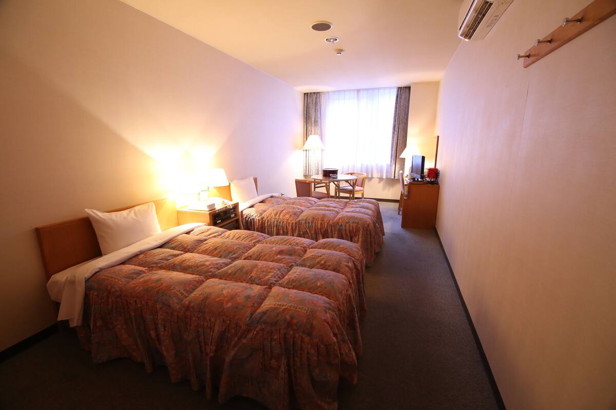 A hotel room with two beds, a desk, a chair, and a window with curtains.
