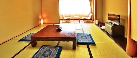 Una habitación con esteras de tatami, una mesa de madera, sillas y una televisión.