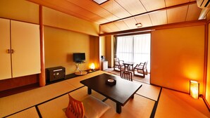 Una habitación japonesa tradicional con suelo de tatami, una mesa baja con cojín, un televisor y una puerta corredera que da a un balcón.