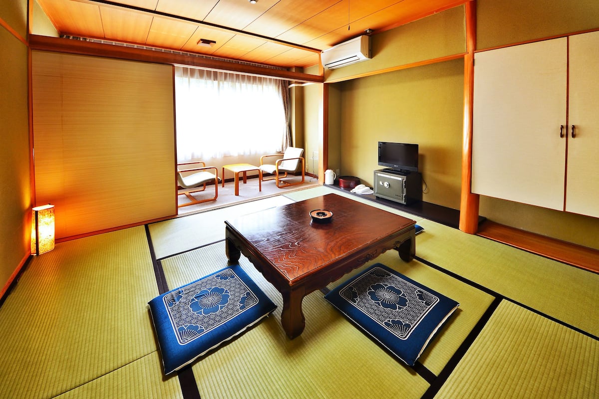 A traditional Japanese room with tatami flooring, a low wooden table, a television, and a cabinet.