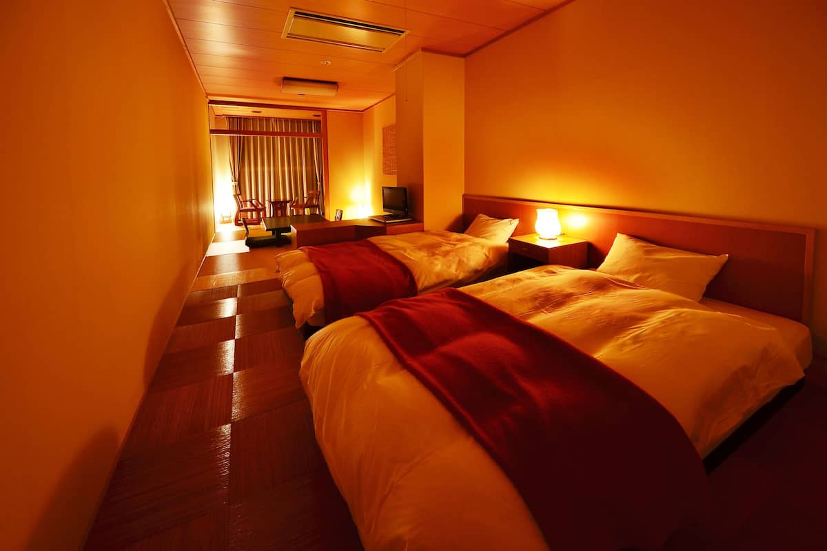 A hotel room with two beds, a television, and a desk with a lamp.