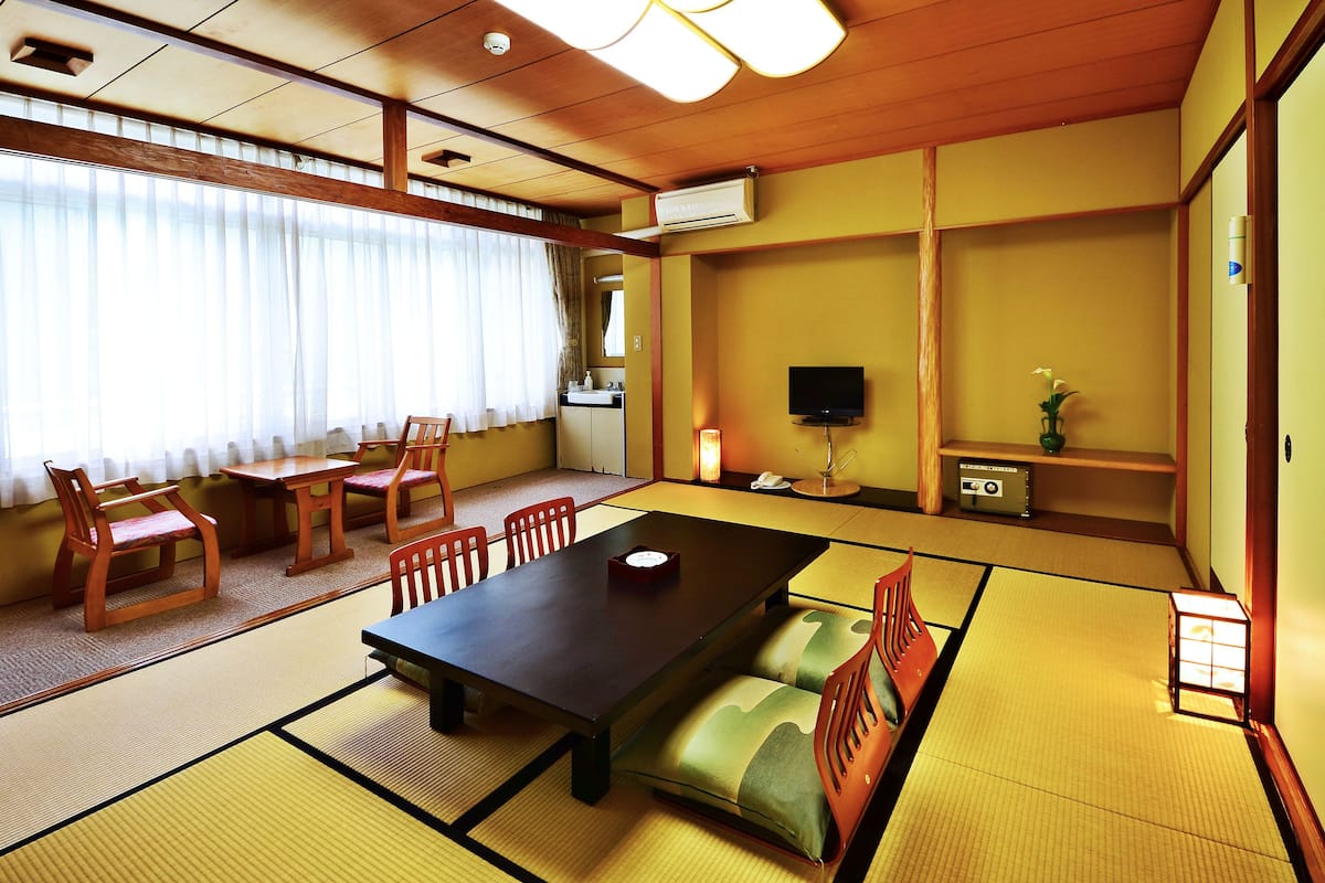 A traditional Japanese room with tatami flooring, a low table, and wooden chairs.
