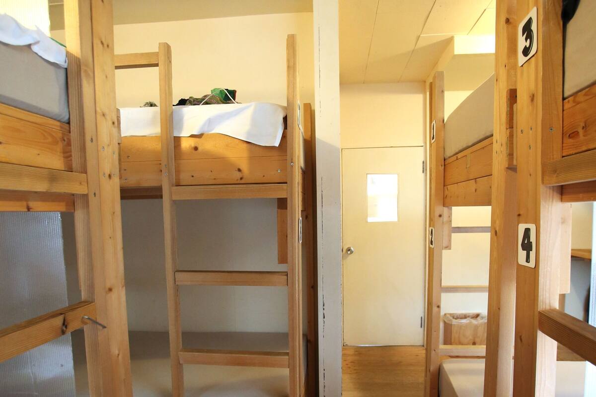 A narrow corridor with bunk beds, wooden walls, and a door at the end.