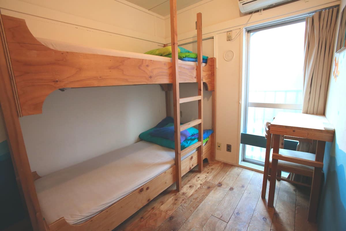 A bunk bed with a ladder, a small table, and a window with curtains.