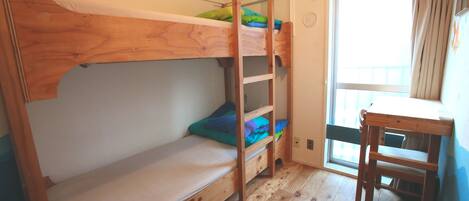 Una cama litera con escalera, una mesita pequeña y una ventana con cortinas.