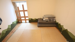 A tatami mat room with a sliding door, a bed with pillows, and a small table with a remote control. - Yadoya Guesthouse Green - Hostel (Tokyo)