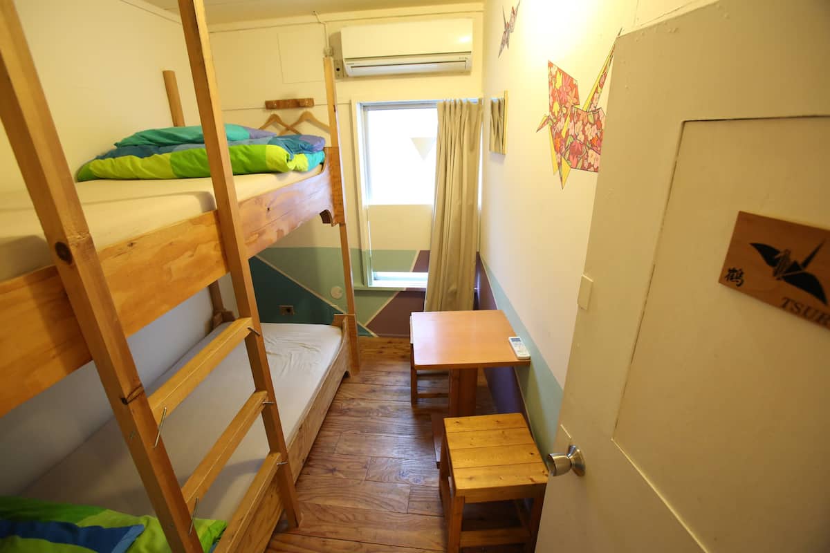 A dormitory room with bunk beds, a small table, and a door with a poster.
