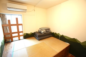 Ein Raum mit Tatami-Matten, einem Futon-Bett, einem Kissenhaufen und einer Schiebetür mit Holzgitterwerk.