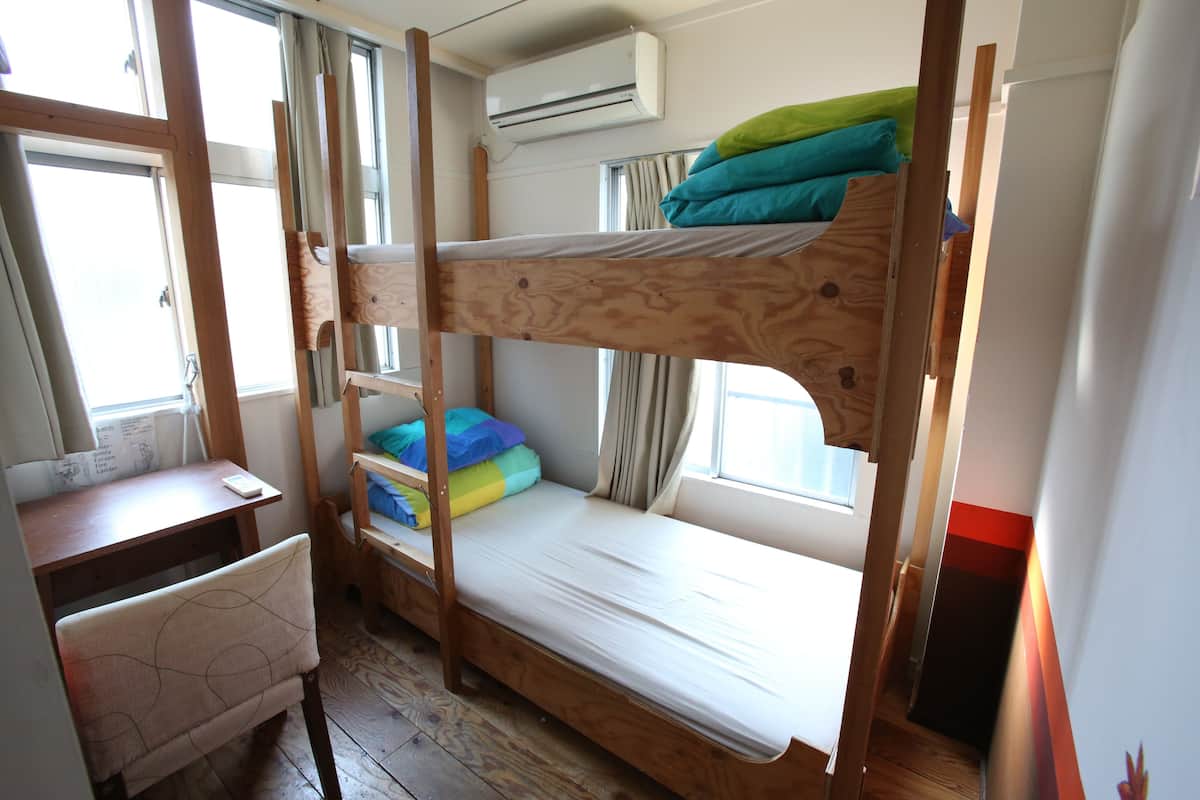 A bunk bed room with a desk and chair, an air conditioning unit, and a window with curtains.