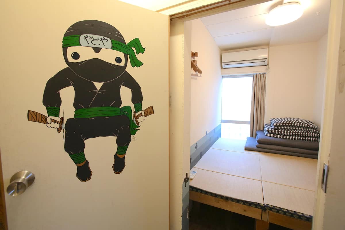 A room with a bunk bed, a wall with a ninja-themed decoration, and a window with curtains.
