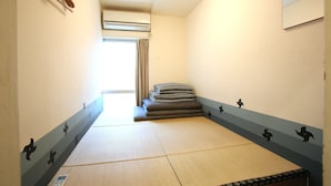 A room with tatami mats, a stack of futons, a mirror, and a wall-mounted air conditioner. - Yadoya Guesthouse Green - Hostel (Tokyo)