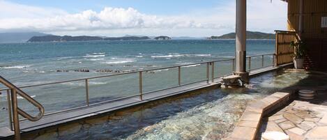 A stone pool with a metal railing overlooking a body of water and distant islands.
