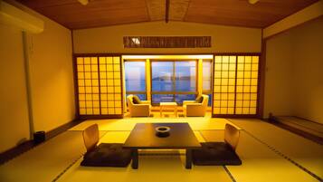 Une pièce de style japonais traditionnel, avec un sol recouvert de tatamis, une table basse, des coussins et une vue sur la mer à travers des paravents en papier.
