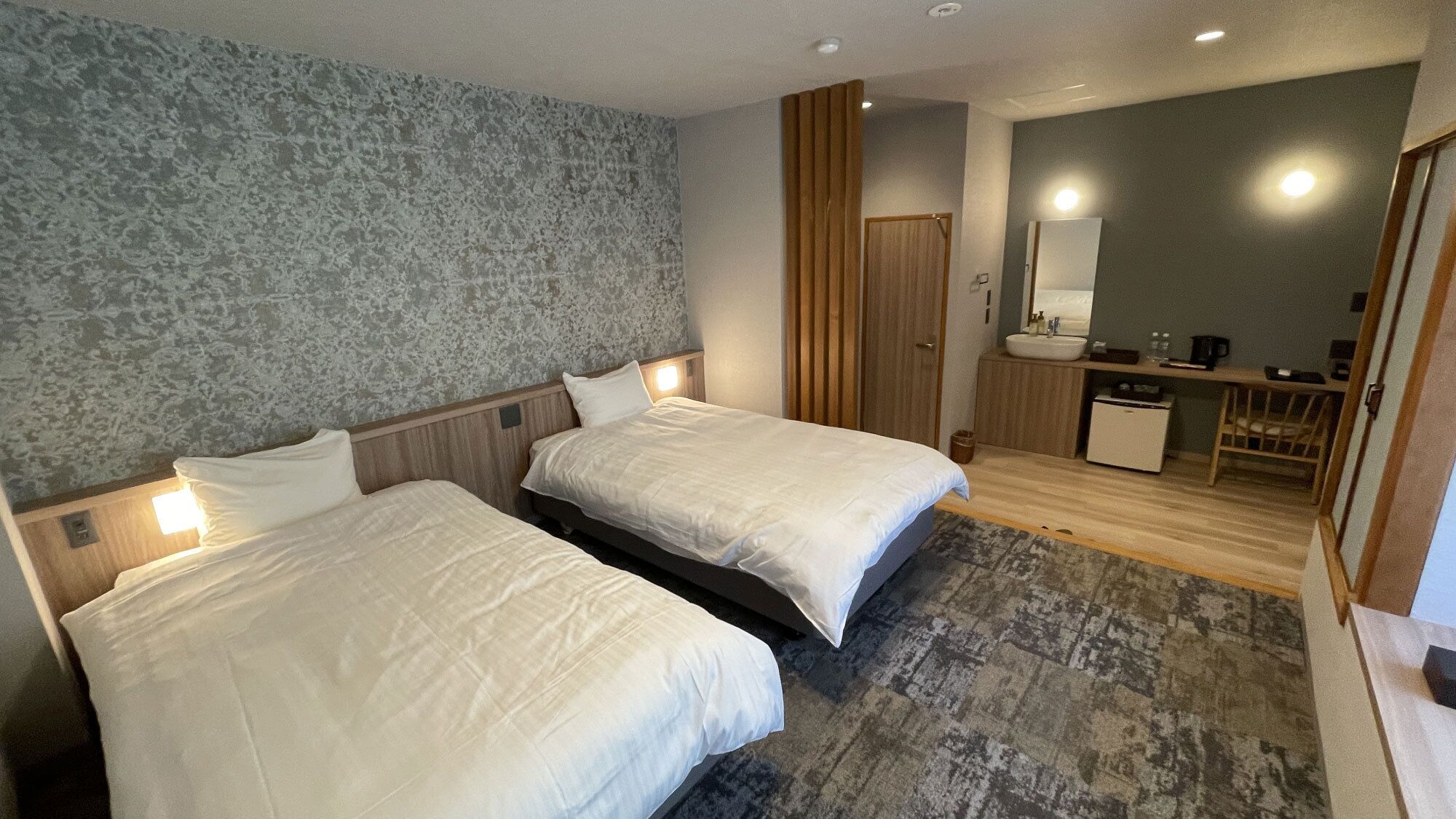 Ein Hotelzimmer mit zwei Betten, einem Badezimmer, einem Schreibtisch und einem Spiegel.