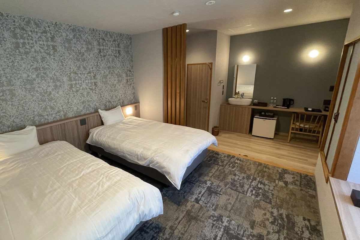 A hotel room with two beds, a bathroom, a desk, and a mirror.