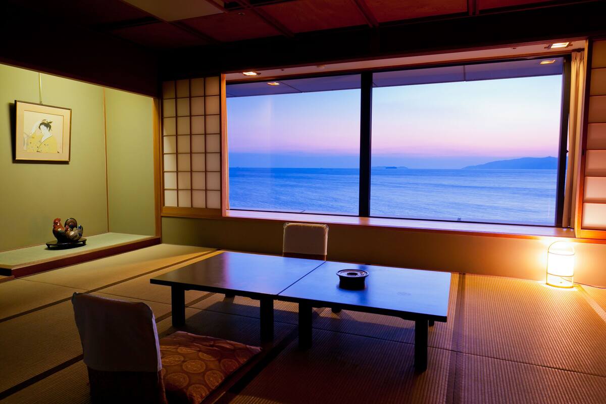 Habitació japonesa tradicional amb fusteria de tatami, una taula baixa i vista al mar al capvespre.