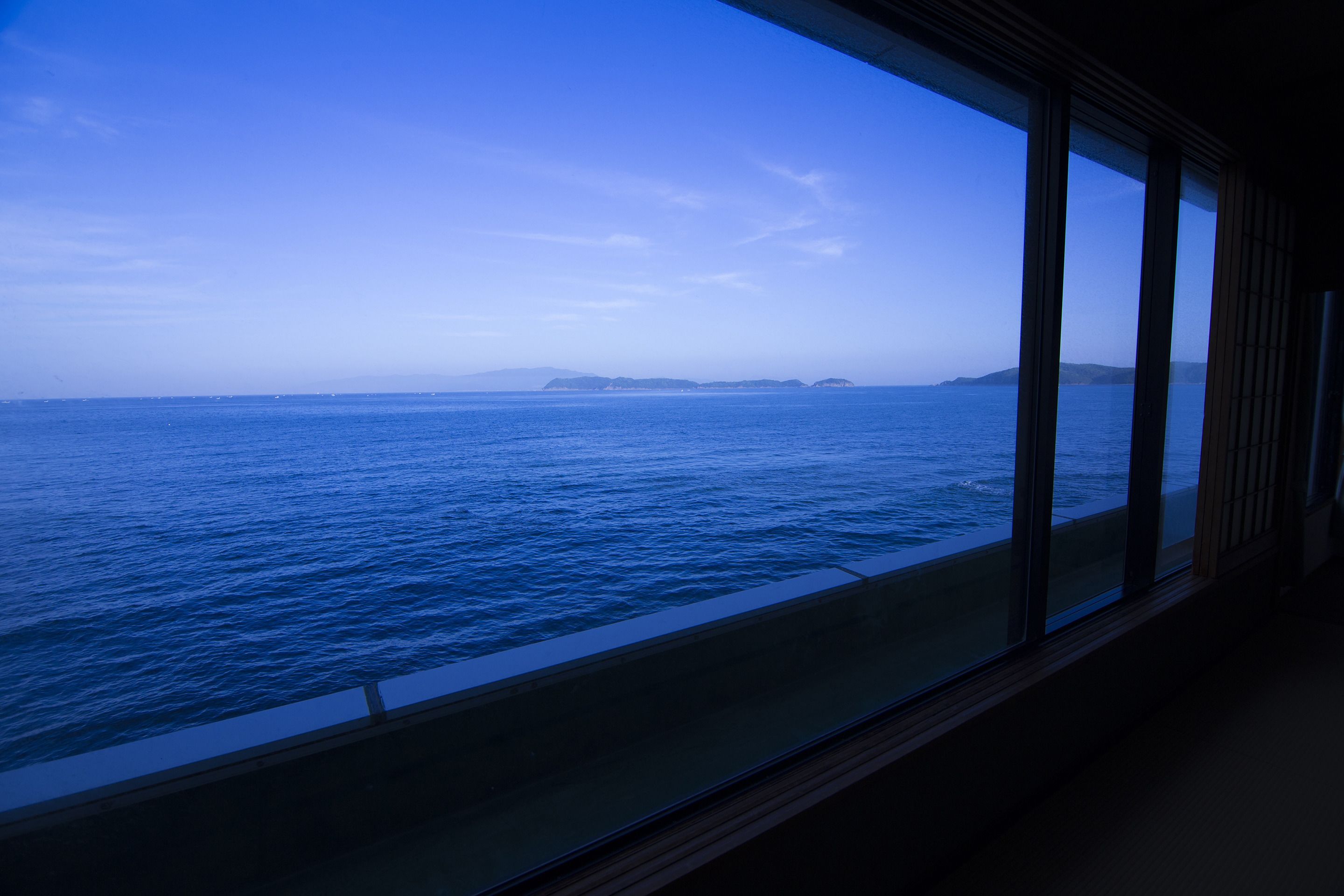 Vista desde una ventana sobre un mar tranquilo con formas de tierra en la distancia.